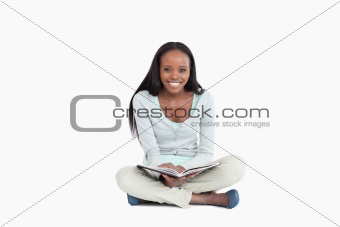 Smiling young woman sitting on the floor with a book