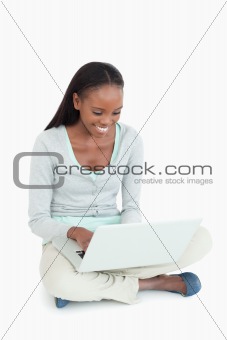 Smiling woman working on her laptop sitting on the floor