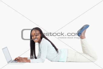 Side view of smiling woman lying on the floor with her laptop