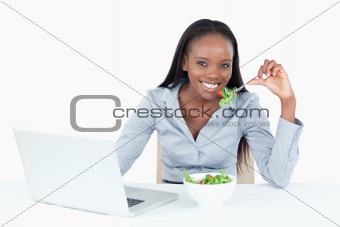 Cute businesswoman working with a notebook while eating a salad
