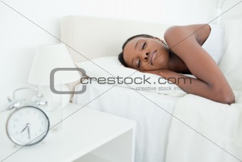 Young woman sleeping while her alarm clock is ringing
