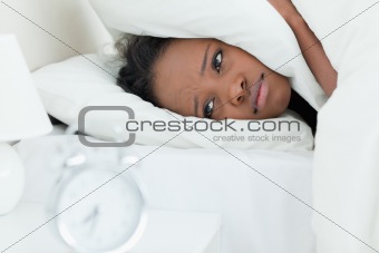 Tired woman covering her ears while her alarm clock is ringing