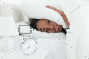 Young woman covering her ears while her alarm clock is ringing