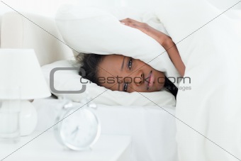 Cute woman covering her ears while her alarm clock is ringing