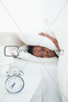 Portrait of a tired woman covering her ears while her alarm clock is ringing