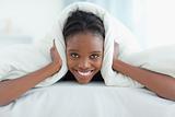 Smiling woman covering her ears with a duvet