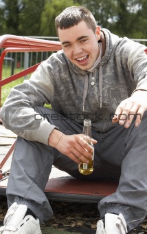 Young Man Sitting In Playground Drinking Beer