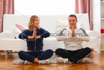Young pregnant woman with husband doing yoga at home

