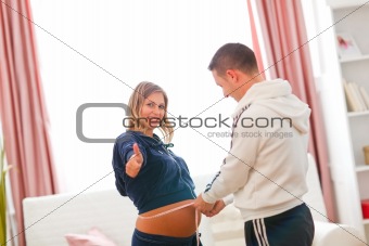 Happy pregnant woman showing thumbs up while husband measuring her tummy 
