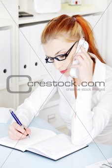 Beautiful businesswoman answering the phone and writing.