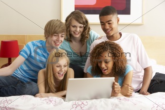 Group Of Five Teenage Using Laptop In Bedroom