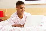Teenage Boy Using Laptop In Bedroom
