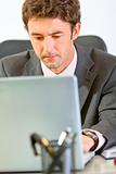 Portrait of modern businessman sitting at office desk and working on laptop
