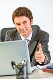 Modern businessman working on laptop and showing thumbs up
