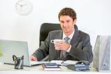 Modern businessman sitting at office desk and having coffee

