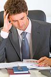 Stressed modern businessman sitting at office desk and working with documents
