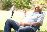 Senior Man Relaxing In Park With Grandchildren In Background