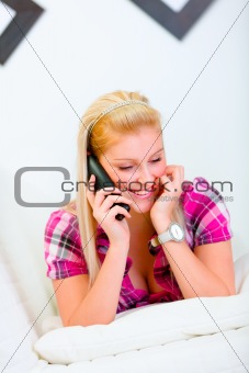 Happy beautiful woman laying on bed and speaking phone
