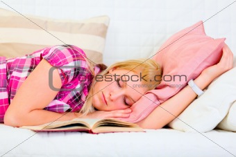 Pretty young woman sleeping on sofa with open book near head
