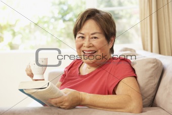 Senior Woman Reading Book With Drink At Home