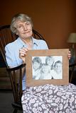Senior Woman At Home Looking At Photo Of Grandchildren