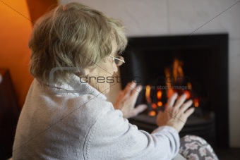 Senior Woman Warming Hands By Fire At Home
