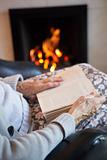 Detail Of Senior Woman Reading Book By Fire At Home