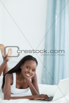 Portrait of a happy woman lying on her belly using a laptop