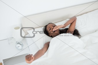 Cute woman yawning and stretching her arms while waking up