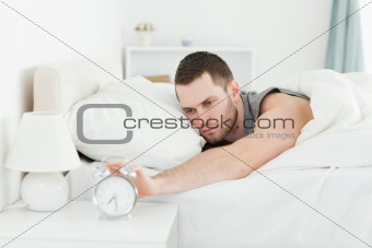 Exhausted man switching off his alarm clock