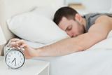 Exhausted man being awakened by an alarm clock