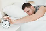 Brown-haired man being awakened by an alarm clock