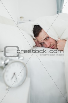 Portrait of a man covering his ears while his alarm clock is ringing