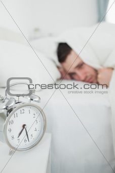 Portrait of a tired man covering his ears while his alarm clock is ringing