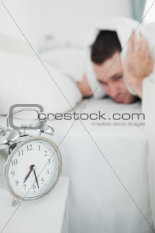 Portrait of a exhausted man covering his ears while his alarm clock is ringing