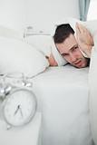 Portrait of a man covering his ears with a duvet while his alarm clock is ringing