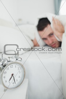 Portrait of a handsome man covering his ears while his alarm clock is ringing