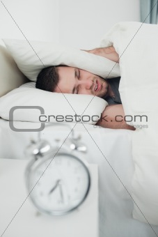 Portrait of a exhausted young man covering his ears while his alarm clock is ringing