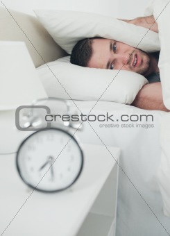 Portrait of a handsome young man covering his ears while his alarm clock is ringing