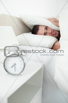 Portrait of an attractive man covering his ears with a pillow