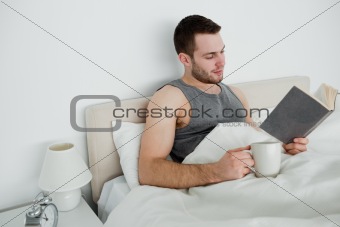 Smiling man reading a novel while having a tea