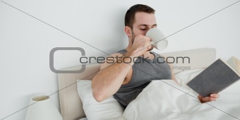 Smiling man reading a novel while drinking a tea