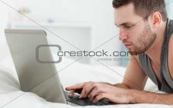 Serious man using a laptop while lying on his belly