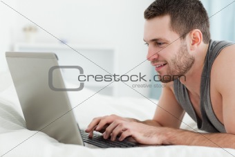 Smiling man using a laptop while lying on his belly