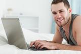 Happy man using a laptop while lying on his belly