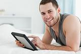 Smiling man using a tablet computer while lying on his belly