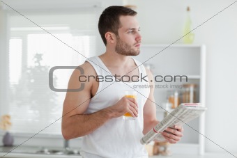 Young man drinking orange juice while reading the news