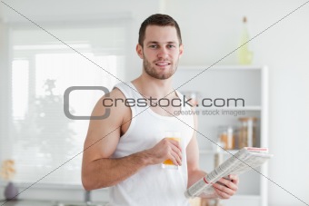 Smiling man drinking orange juice while reading the news