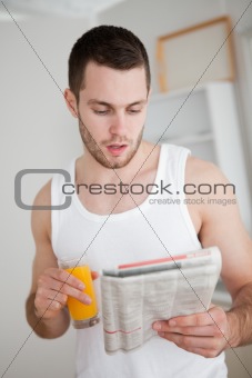 Portrait of a young man reading the news while drinking orange juice