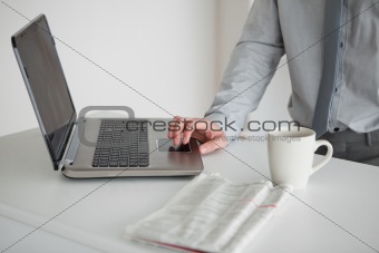 Businessman using a laptop with a cup of tea and a newspaper
